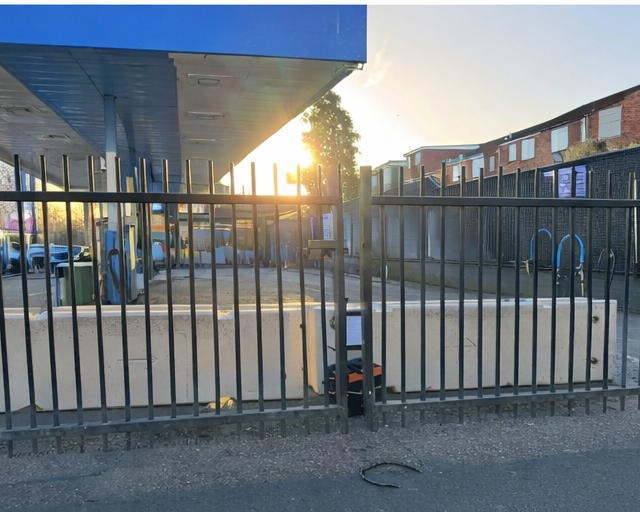 Concrete security barriers installed behind metal fence at commercial property during early morning work.