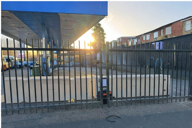 Concrete security barriers installed behind metal fence at commercial property during early morning work.